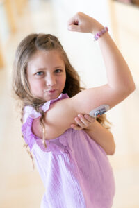 Little girl flexing her bicep muscle with a continuous glucose monitor on her arm